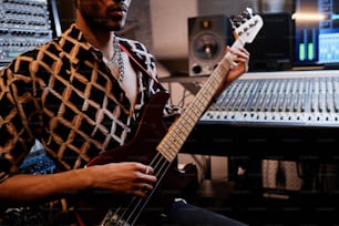 Colpo di sezione media di un giovane musicista rock nero elegante che suona la chitarra elettrica in studio di registrazione