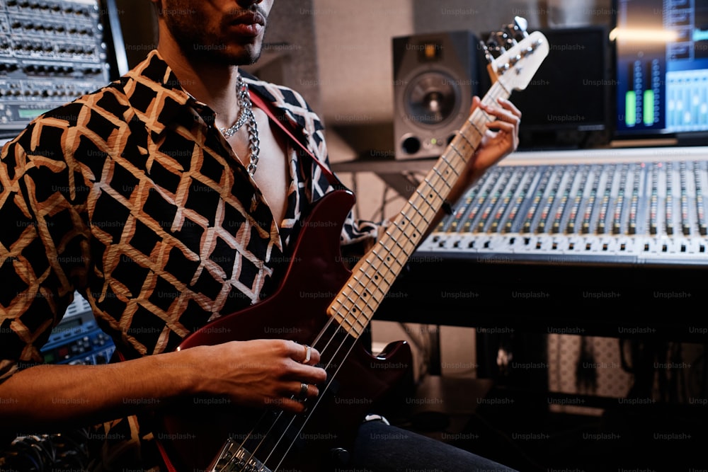 Plano de sección media de un joven músico de rock negro con estilo tocando la guitarra eléctrica en un estudio de grabación