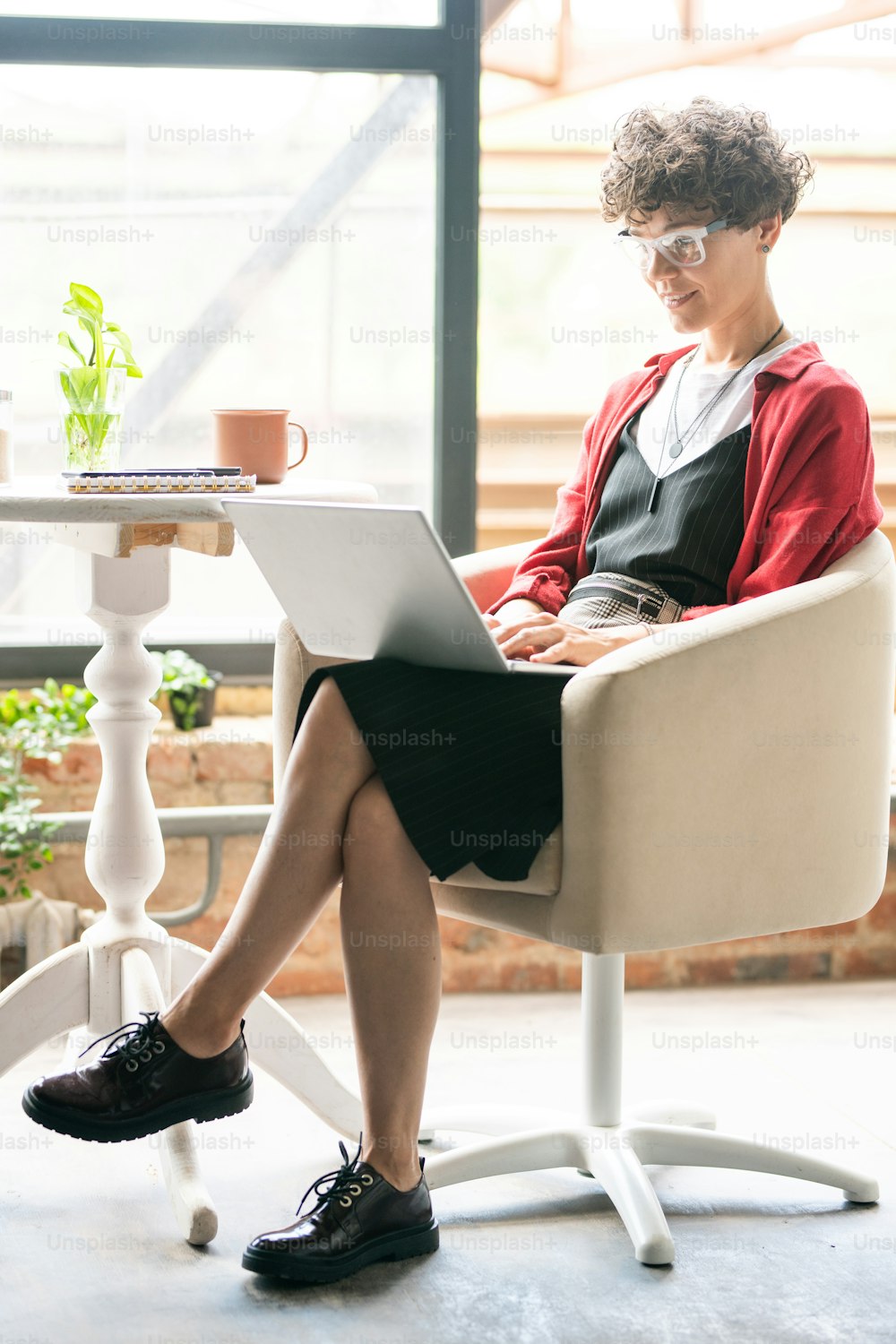 Young elegant businesswoman doing computer work while sitting in armchair with laptop in front inside office