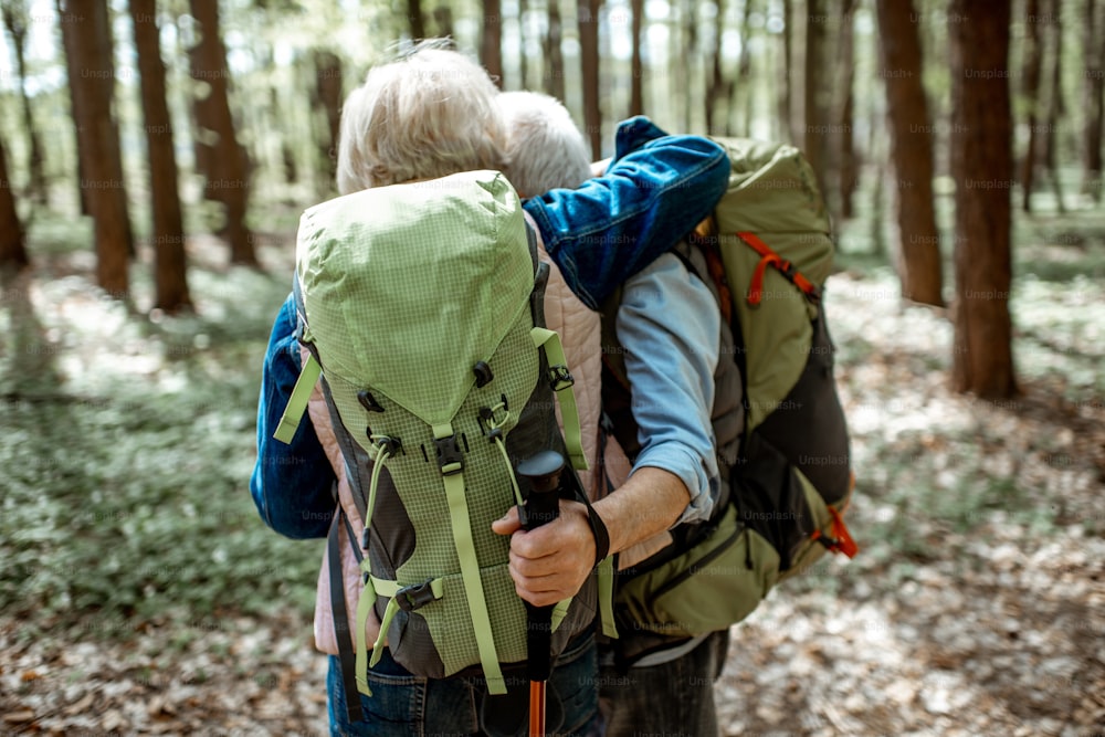 Adorável casal sênior abraçando na floresta enquanto caminha com mochilas, vista para trás