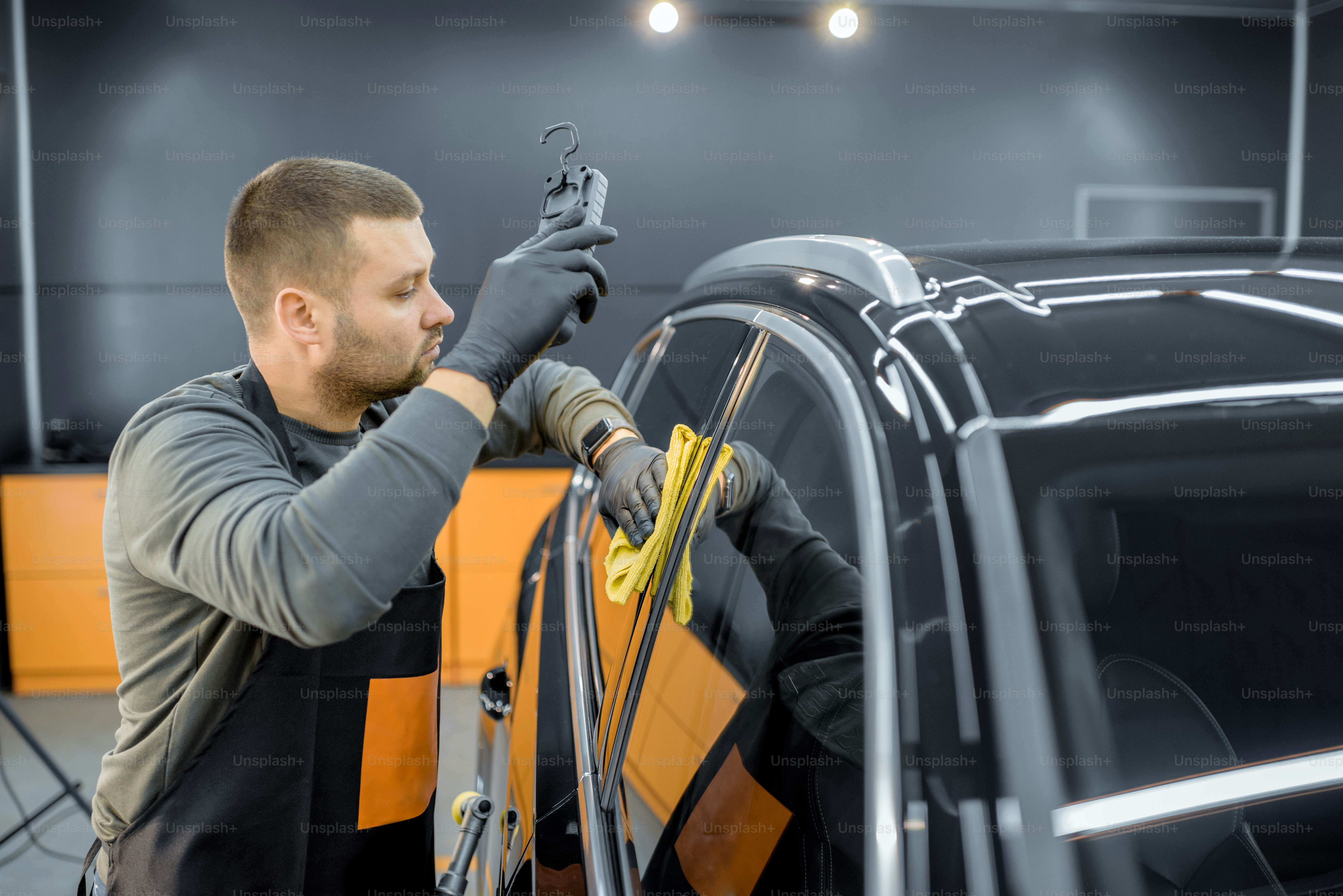 Autowerkstatt wischt die Fahrzeugkarosserie mit Mikrofaser ab und untersucht die glänzende Beschichtung nach dem Poliervorgang. Professionelles Fahrzeugdetaillierungs- und Wartungskonzept