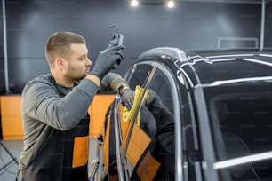 Car service worker wiping vehicle body with microfiber, examining glossy coating after the polishing procedure. Professional car detailing and maintenance concept