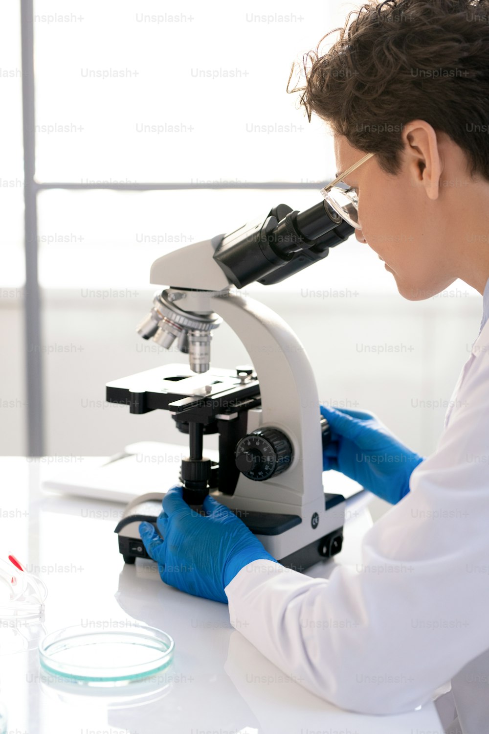 Vista sopra la spalla del ricercatore di laboratorio concentrato che utilizza il microscopio mentre lavora con il campione medico in laboratorio