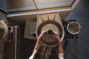 Artigiana che usa le mani per modellare un pezzo di argilla bagnato che gira su una ruota mentre lavora nel suo laboratorio di ceramica