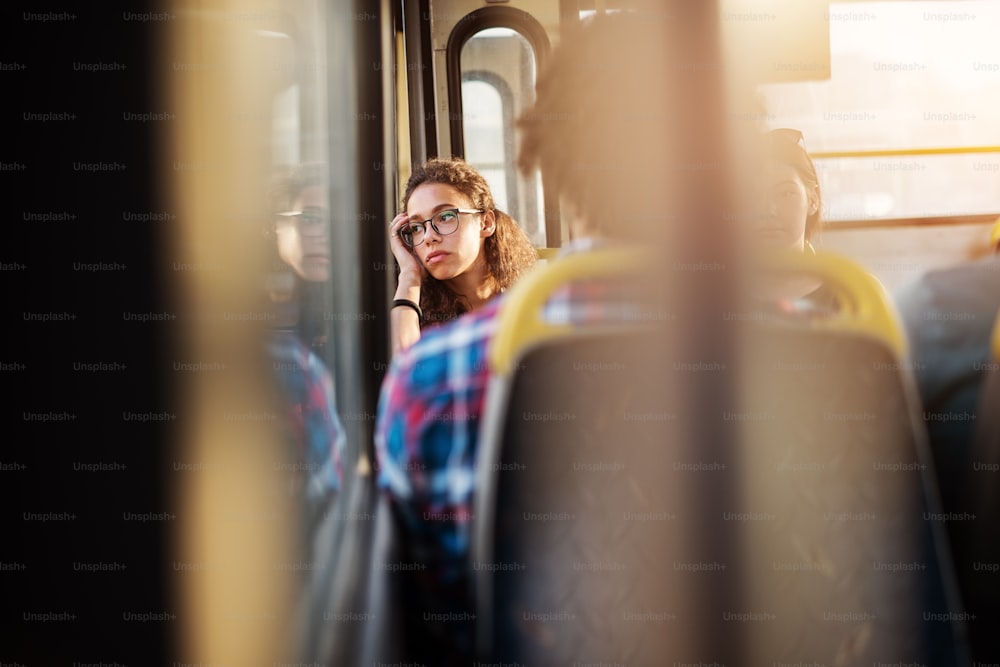 A young pretty bored woman is sitting in a bus seat leaned and looking through the window as she waits for long trip to end.
