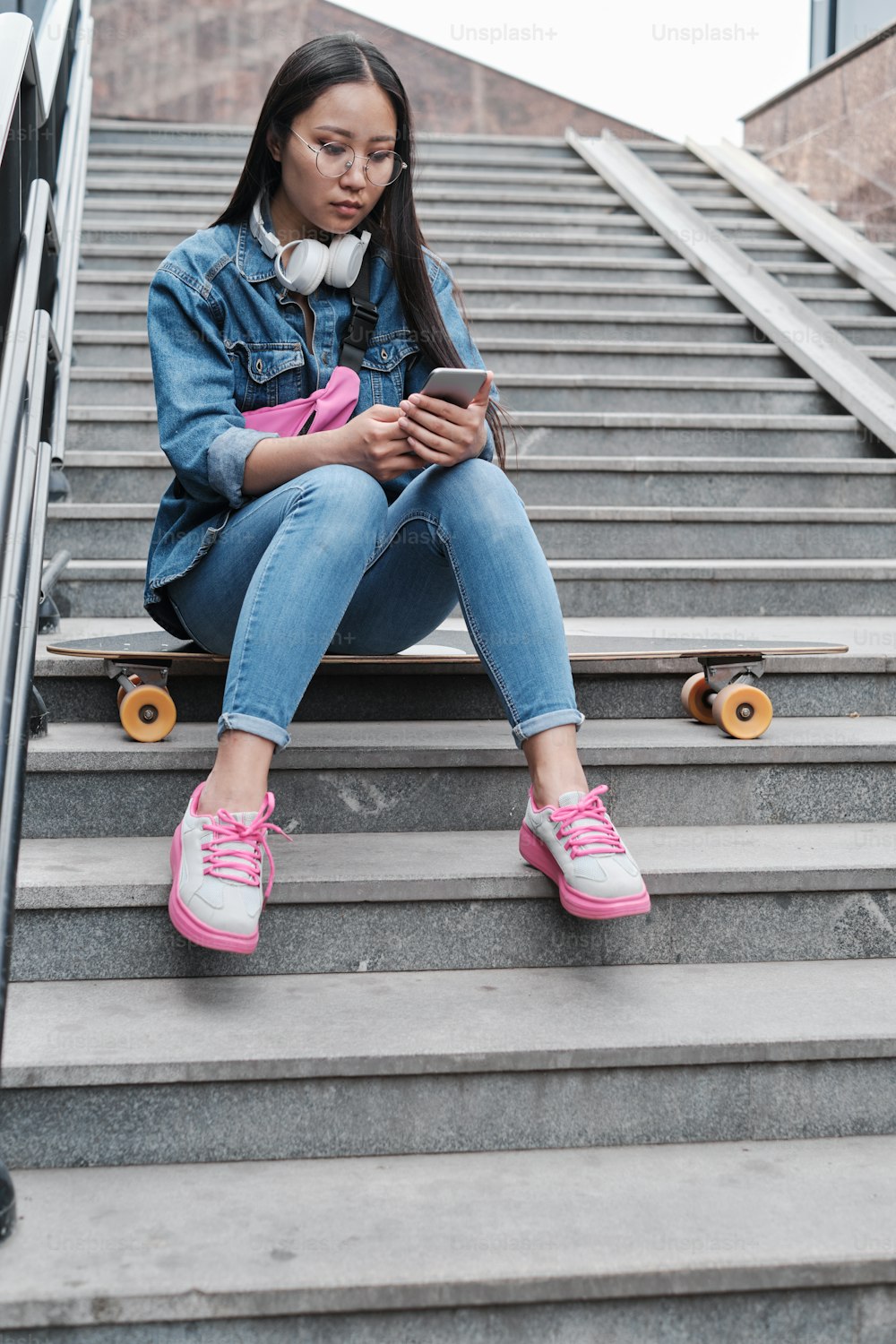Girl with a longboard sits on the stairs and looks at her phone screen.