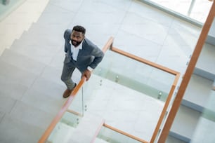 High angle view of serious Afro-American bearded businessman in suit moving up stairs and looking at camera