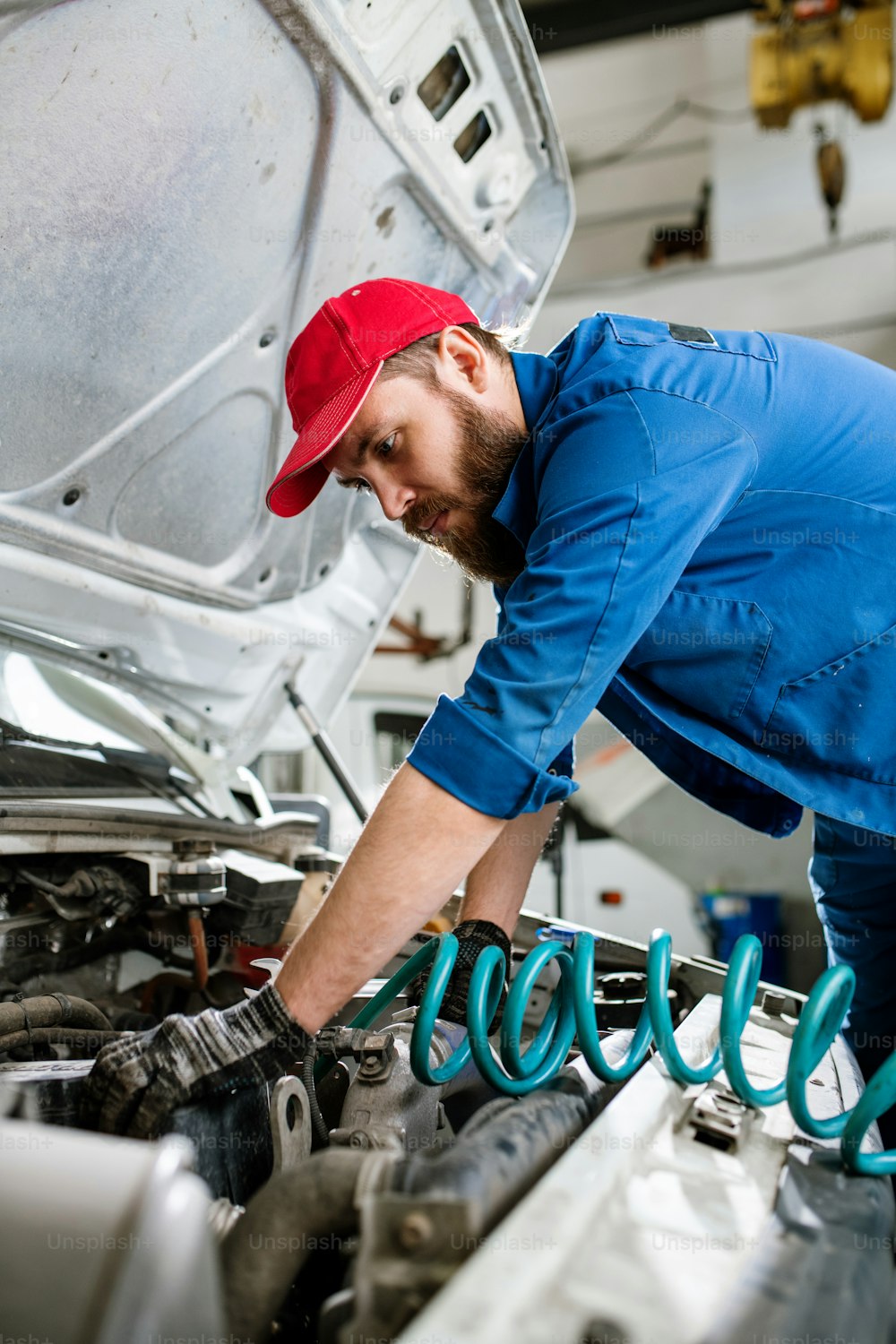 Serious young bearded engineer of machine maintenance service bending over engine of large vehicle during work