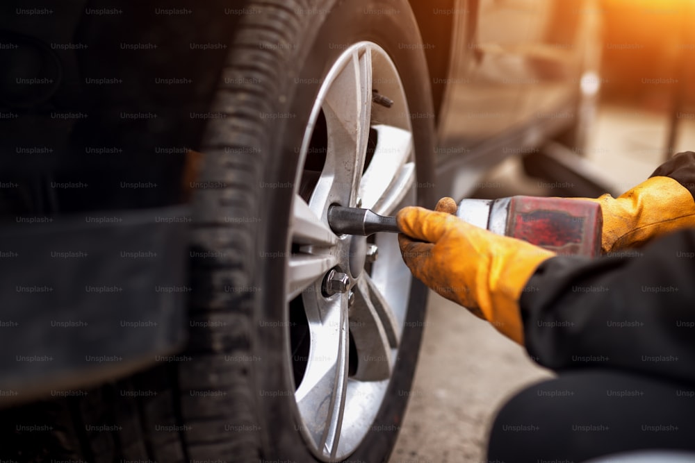 Homem mecânico de automóveis com chave de fenda elétrica trocando pneu do lado de fora. Serviço de carro. As mãos substituem os pneus sobre rodas. Conceito de instalação de pneus.