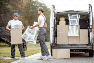 Delivery company employees unloading cargo van vehicle, delivering some goods and furniture to a clients home. Relocation and professional delivery concept