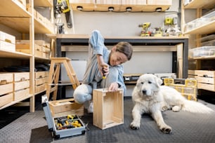Una joven manitas hace cajas de madera, sentada en el suelo con su lindo perro en el taller bien equipado de su casa