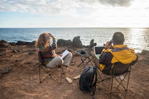 nice couple enjoying a sunset at the end of the day. travel lifestyle in wanderlust for happy caucasian people. working alternative office with laptop and mobile connection to internet. photographers and tourist