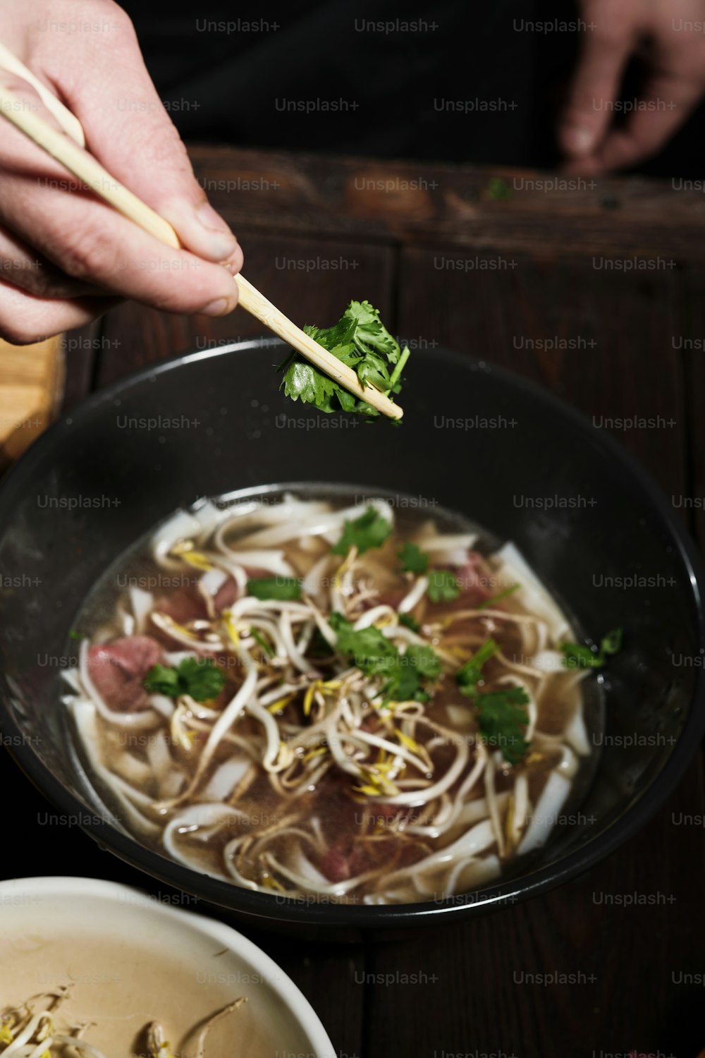 Close up of chef's hands grabbing parsley, adding to a bowl of pho bo with beef