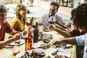 Gruppe von Freunden, die Spaß beim Grillabend im Freien im Gartenrestaurant haben - Gemischtrassige Menschen, die Essen beim Grillen im Hinterhof essen - Freundschafts-, Jugend- und Partykonzept