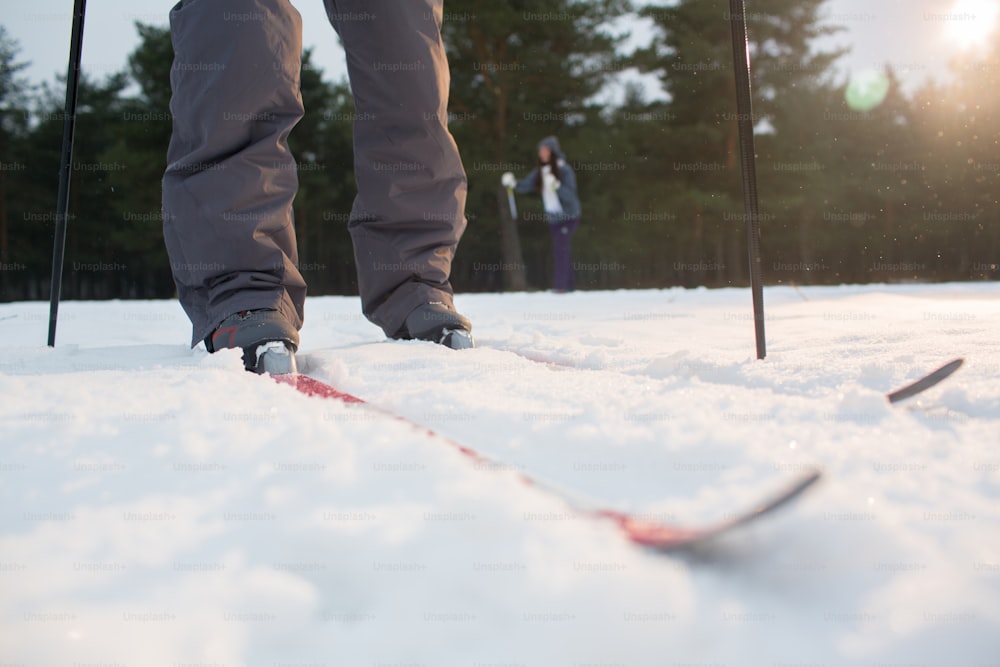 Piernas de humano de pie sobre esquís y moviéndose hacia adelante por la pista de esquí en la nieve