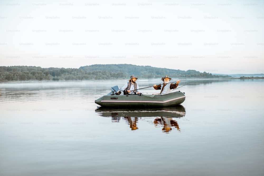 Nonno con figlio adulto che pesca sul gommone sul lago con acqua calma la mattina presto. Ampia vista panoramica