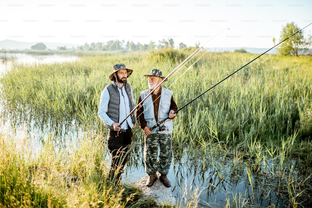 Grandfather with adult son fishing on the lake, standing together between the reeds during the morning light