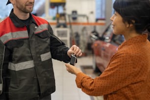 Close up of mechanic giving car keys to female client after finishing repairs and maintenance in auto shop, copy space