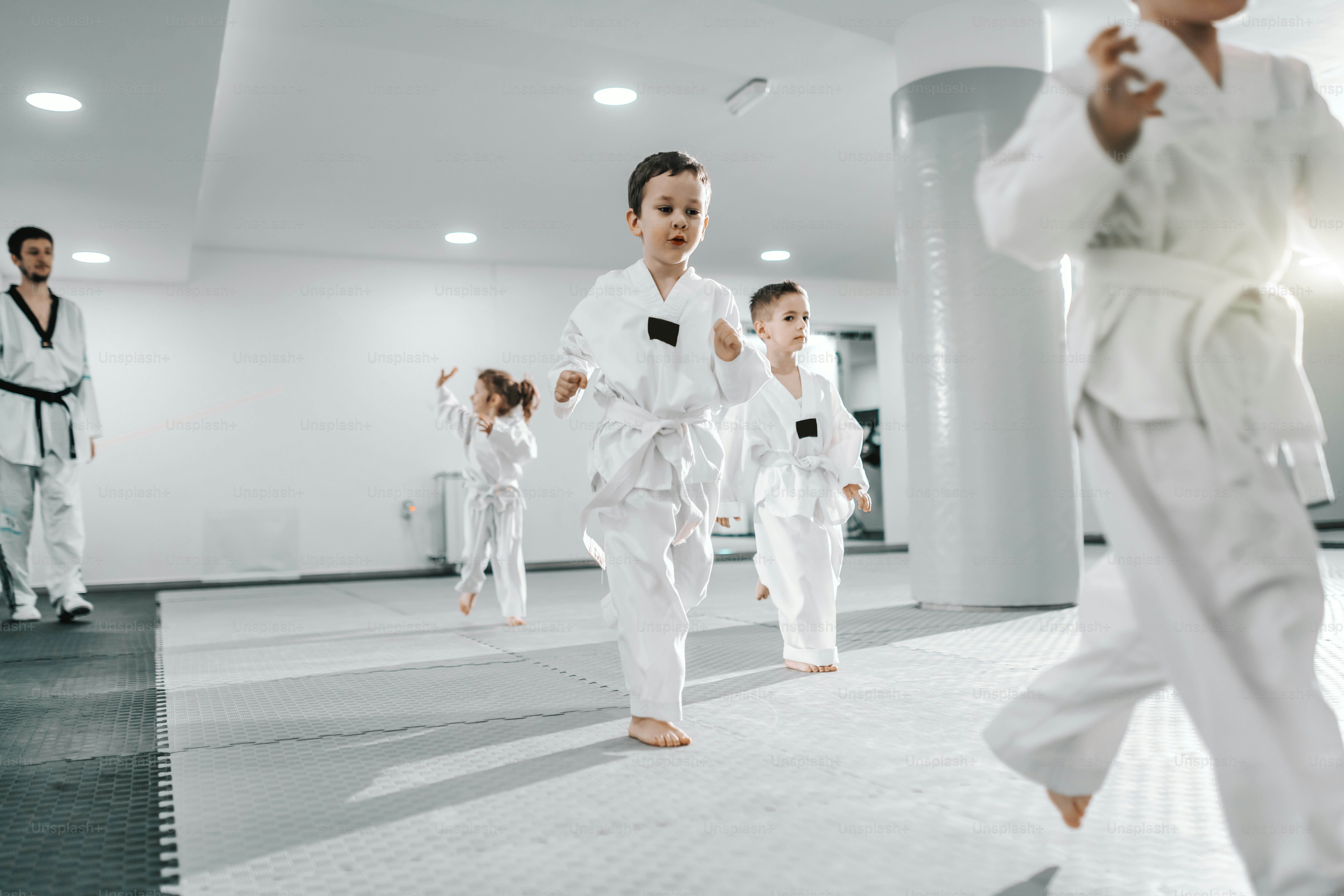Pequeño grupo de niños entrenando en la clase de taekwondo. Todos vestidos con doboks. Fondo blanco