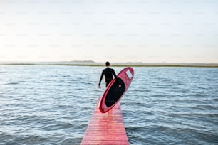 Landschaftsansicht auf dem See mit Mann mit Paddleboard auf dem Pier während des Sonnenaufgangs
