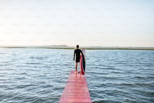 Vista del paisaje en el lago con el hombre de pie con la tabla de remo en el muelle durante el amanecer
