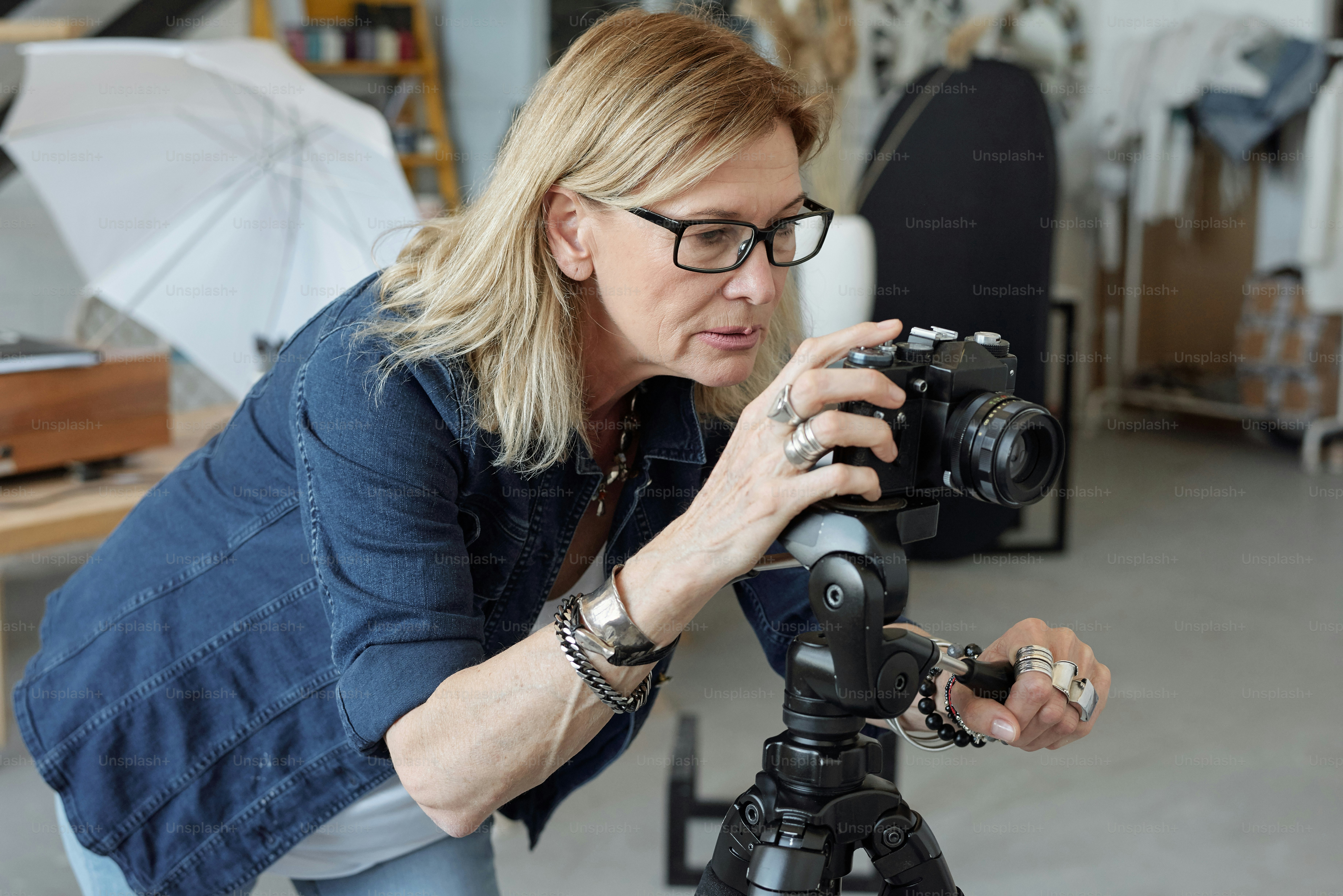 Concentrated mature photographer in eyeglasses looking through camera ...