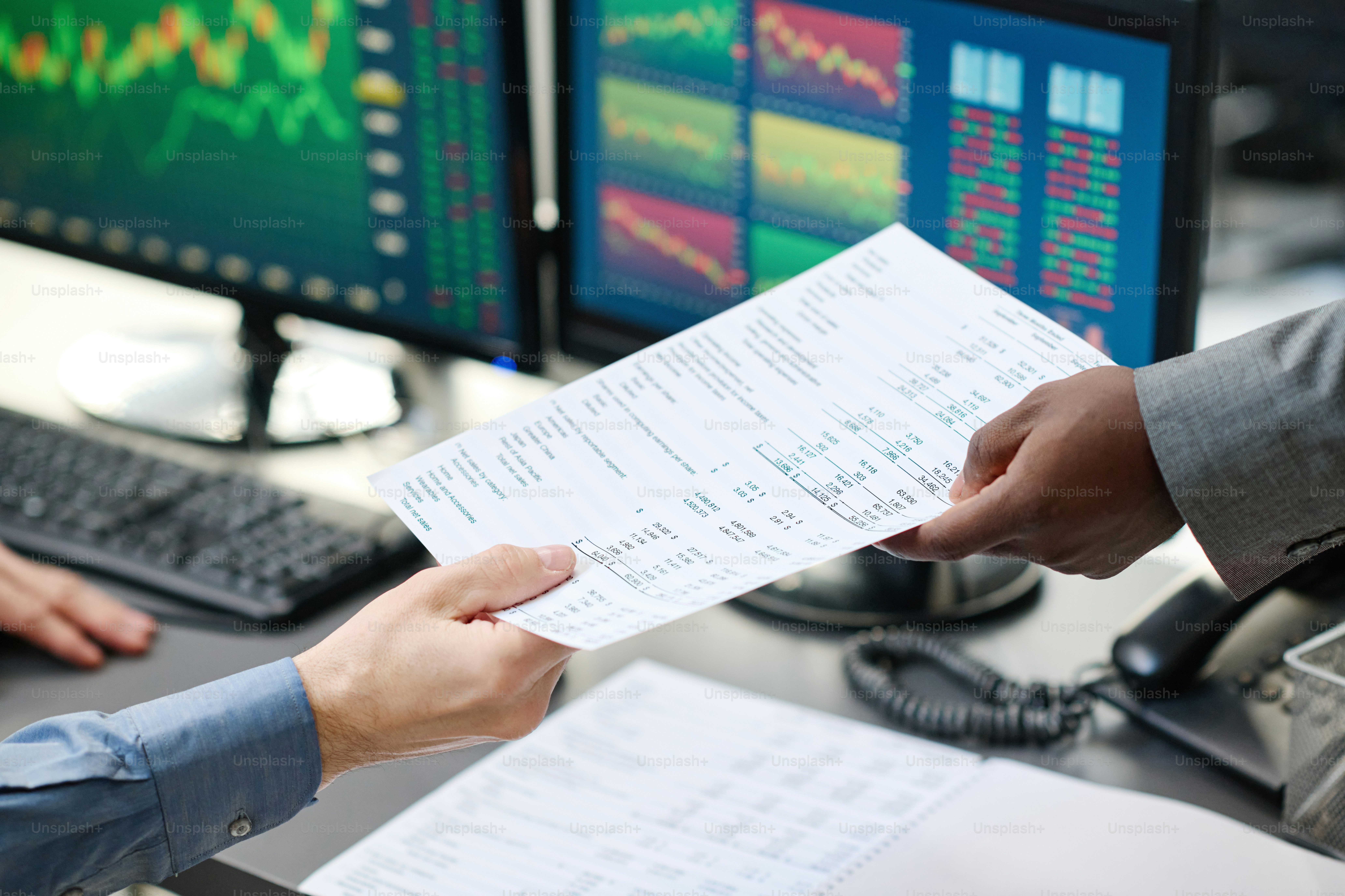 Unrecognizable African American broker delivering papers to his busy Caucasian colleague sitting in front of computers