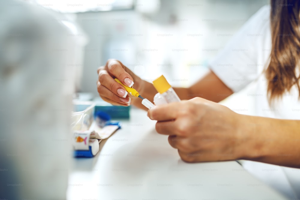 Close up of female laboratory assistant preparing needle and test tubes for blood sampling.