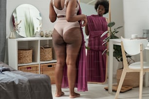 Vista trasera de una mujer joven de talla grande que se prueba un vestido nuevo frente al espejo en el dormitorio