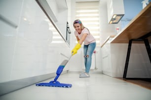 A woman doing chores, sweeping kitchen floor with mop.