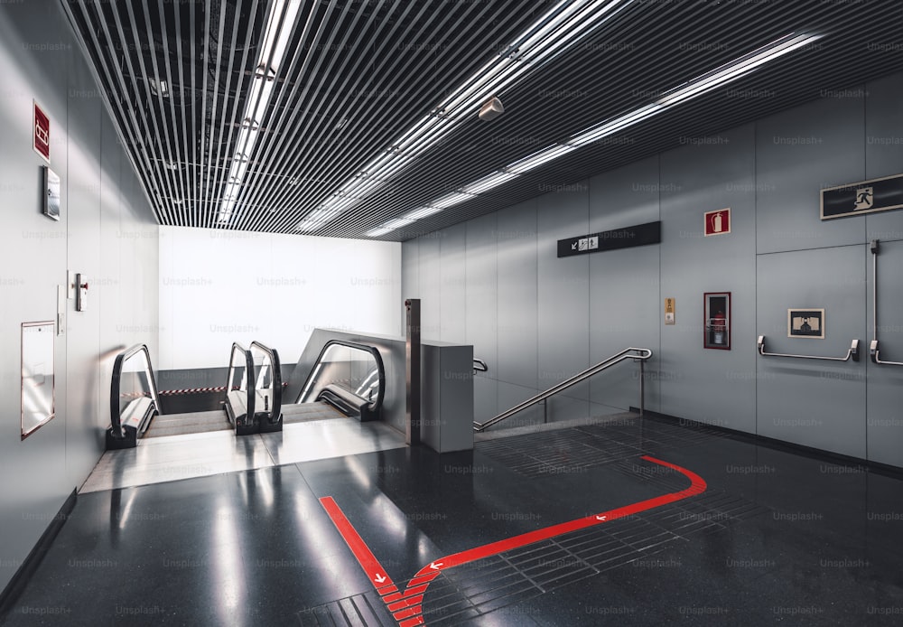 Contemporary escalator and staircase indoors of an airport terminal Barcelona El Part BCN, with a red line with arrows on the floor, emergency exit, and soundproof ceiling