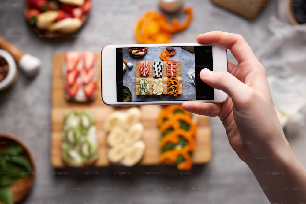 スマートフォンでヘルシーな作りたてのサンドイッチの写真を撮る女性の接写、上面図