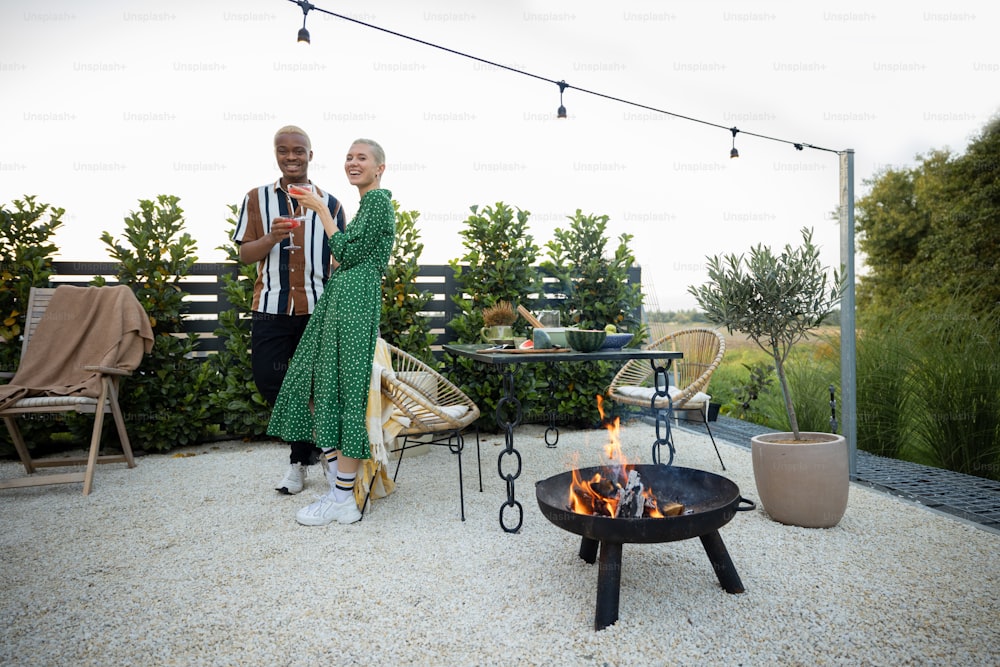 Multiracial couple hanging out together during a dinner at their backyard in the evening. Standing with drinks. Concept of relationship. Black man and european woman enjoying time together