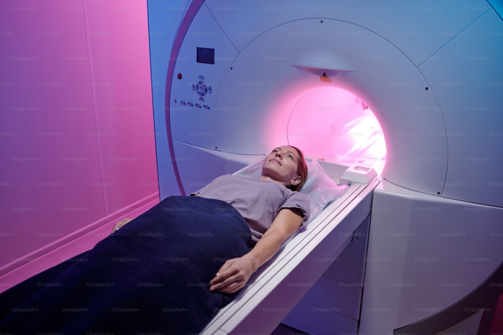 Young female patient lying on long table of mri scan machine while undergoing medical examination