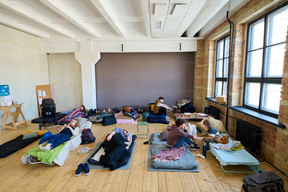 Varios lugares para dormir con personas temporalmente sin hogar que descansan y se comunican entre sí en una habitación espaciosa