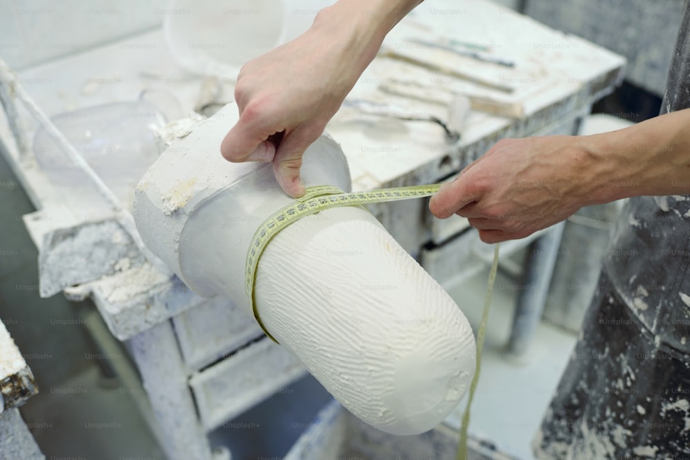Mãos de jovem trabalhador da fábrica de próteses segurando fita métrica de gesso redondo molde enquanto trabalhava sobre a prótese nova