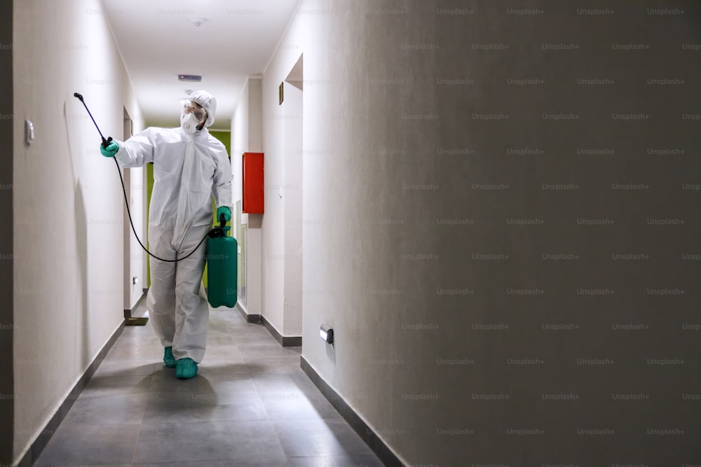 コロナウイルス/covid 19から建物の滅菌ホールに無菌スーツとマスクを着た労働者。