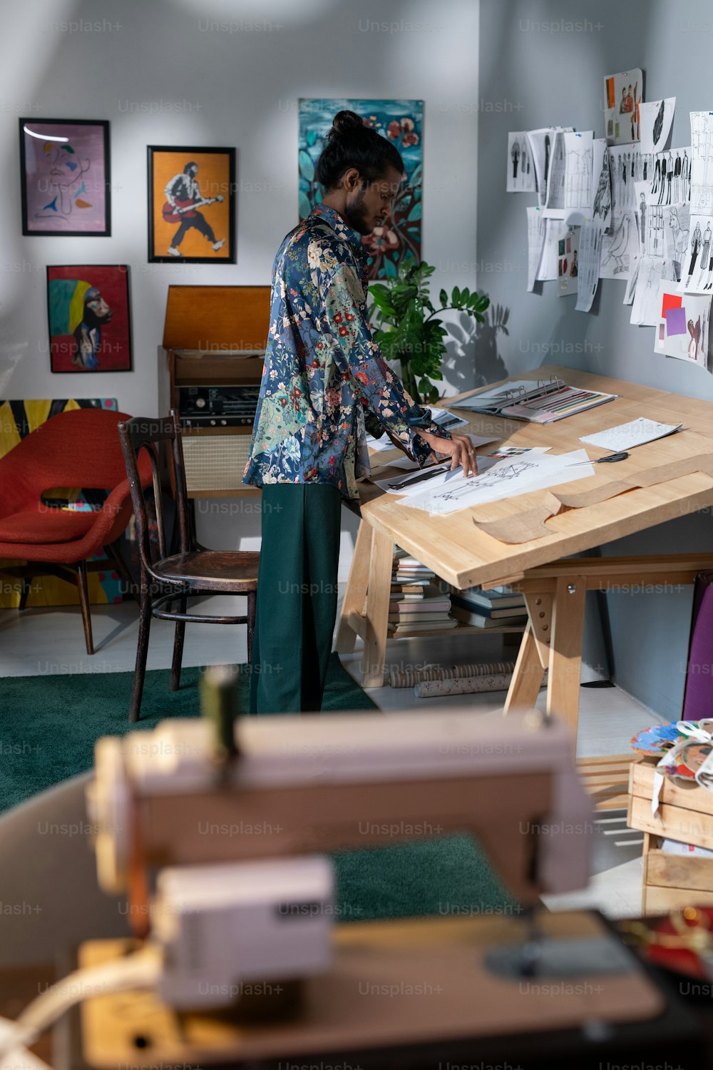 Jovem criativo de pé ao lado da mesa de madeira com suas obras de arte e procurando os melhores desenhos para exposição de artes modernas