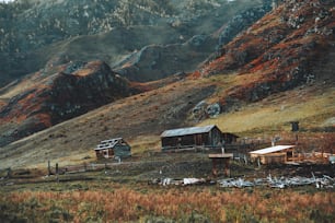 Várias cabanas de madeira semiabandonadas e currais de gado nas montanhas de Altai, na Rússia, com cercas envolvendo pastagens e prados cobertos de gramíneas nativas, uma cordilheira de colina de outono ao fundo