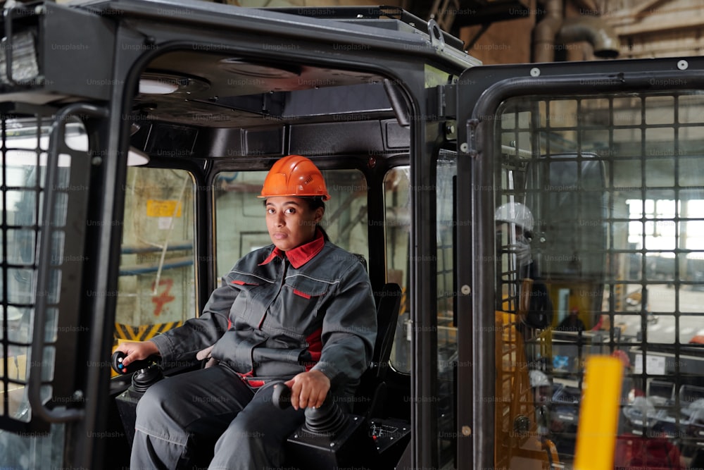 Constructeur portant un casque de sécurité et des vêtements de travail assis dans la cabine d’une machine de construction et la conduisant tout en gardant les mains sur les changements de vitesse