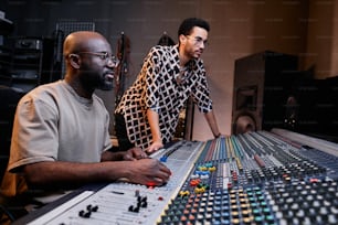 Moderner, reifer schwarzer Toningenieur und stilvoller junger Sänger, der im Aufnahmestudio an einem Musiktitel arbeitet