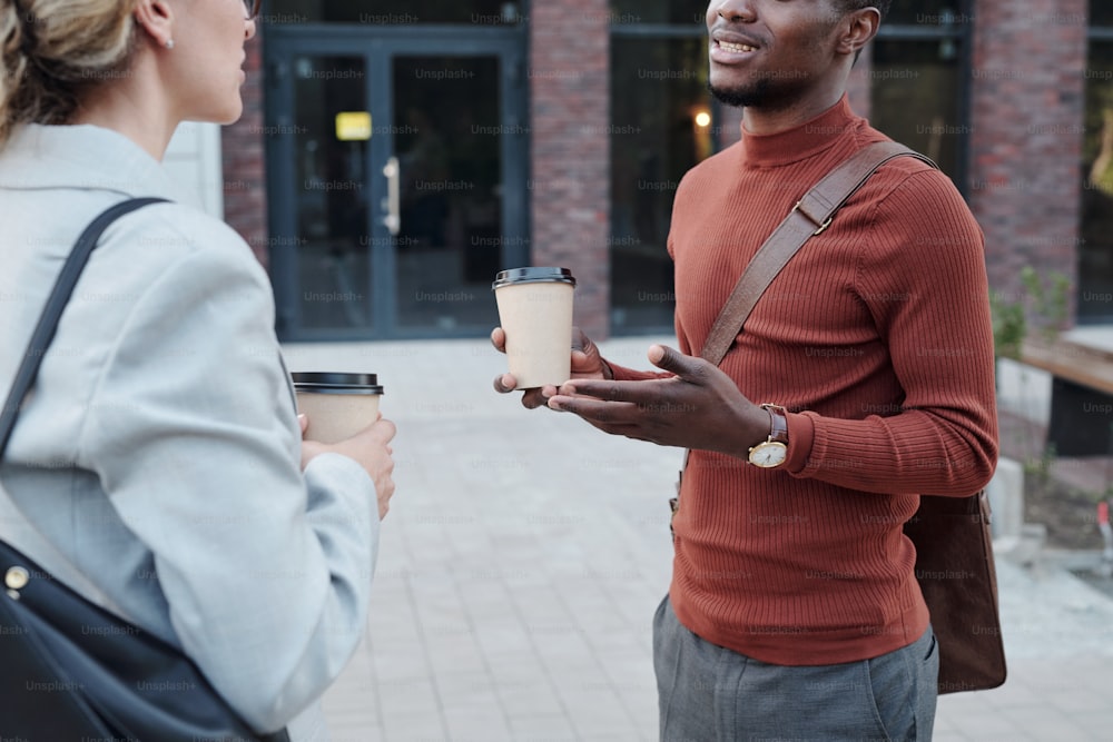 African man and Caucasian woman with drinks talking at coffee break in the street