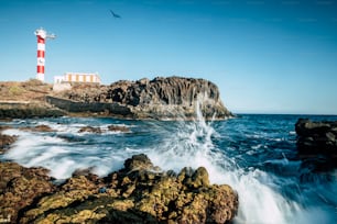 Beautiful scenic landscape with classic lighthouse on the coast and blue ocen and sky in background - concept of travel and vacation for tourism - wave and rocks