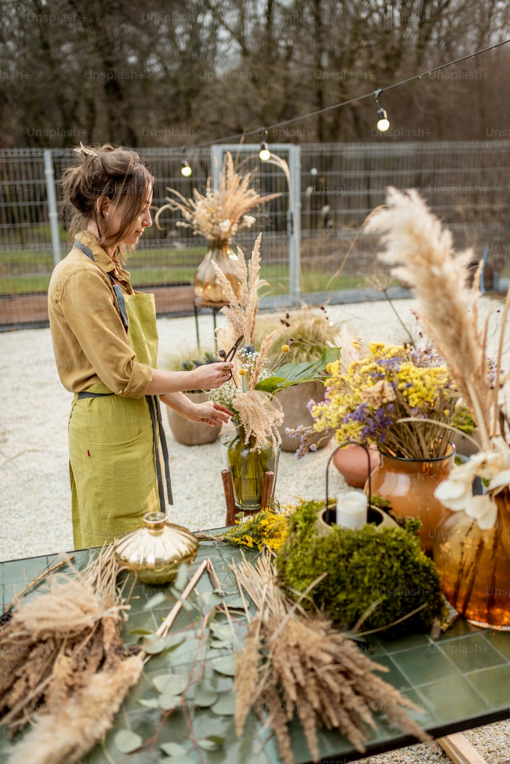 야외 작업장에서 건조하고 신선한 꽃과 허브로 작곡을 하는 젊은 여성. 꽃 장식을 구성하는 꽃집, 정원사 또는 데코레이터