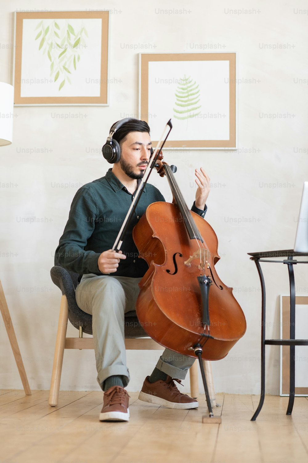 Joven profesor de música con violonchelo sentado en sillón en la sala doméstica y explicando cómo tocar el instrumento musical