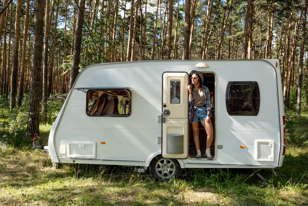 Giovane turista femminile che si leva in piedi nella porta della casa mobile nella foresta