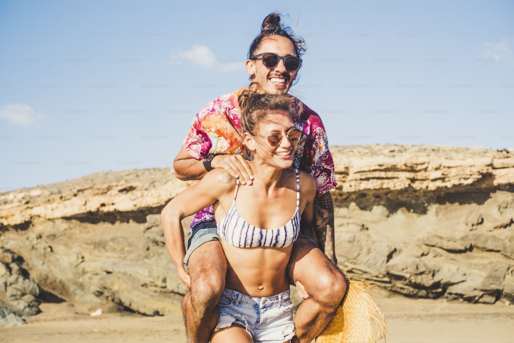 Funny concept with cheerful happy people enjoying the summer vacation at the beach - muscle girl carry the boyfriends on his back - laughing a lot and enjoying the outdoor leisure activity together in relationship