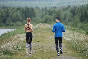 Two mid age man and woman jogging outdoor, warming up muscules, in summer, on gloomy day, at the road with perspective and scenic view, full length, from the back, running away