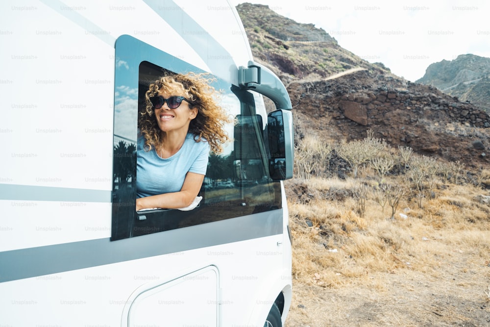 Les gens et le voyage destination de vacances de vacances. Une jeune femme adulte heureuse sourit et profite de la nature hors route pour se garer devant la fenêtre de son camping-car moderne. Voyageuse