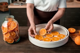 Nahaufnahme einer nicht erkennbaren Hausfrau, die mit einem Glas getrockneter Orangen am Tisch steht und zu Hause eine Obsttrocknermaschine benutzt